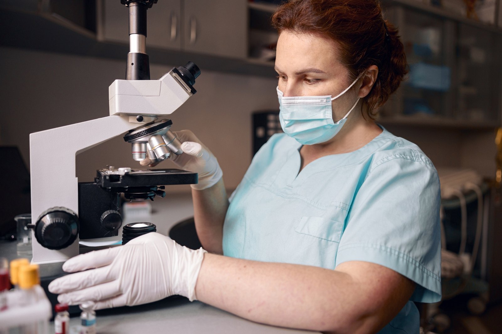 Woman lab assistant works with microscope to research material sample in clinic